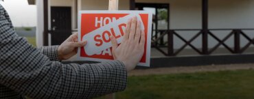 A real estate agent covering up a "Home for Sale" sign with a "Sold" sign.