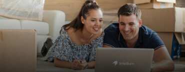 A couple smiling and looking at a computer while on the floor of their new house.