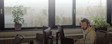 A man wearing headphones and working at a desk in an office.